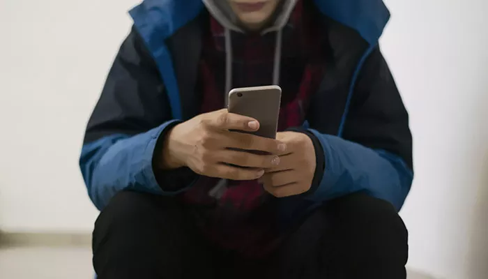 A person in a hoodie holds a phone in their hands. Their face is not visible.