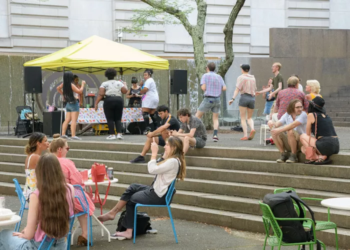 A group of people sit on steps, take selfies, and dance outside of the Carnegie Museum of Art.