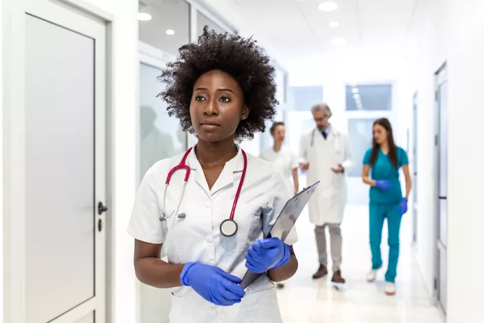 a Black nurse walking down a hallway with other nurses behind her