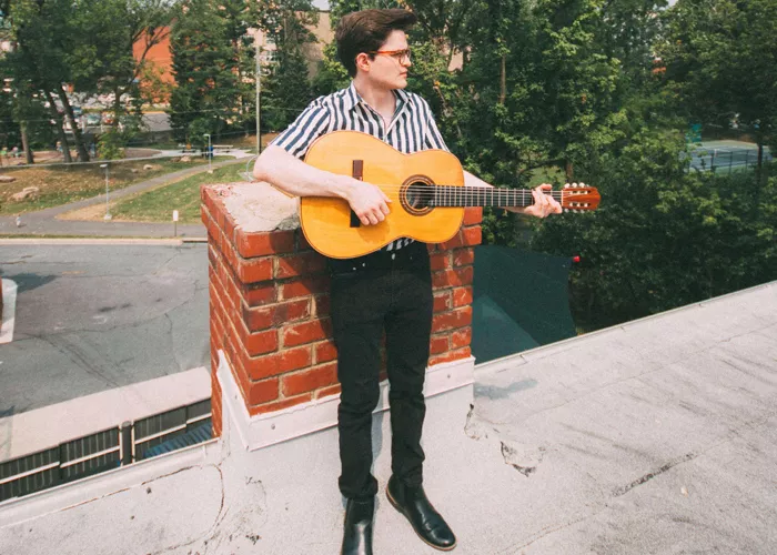 Zack Keim standing in a striped shirt and holding a guitar.