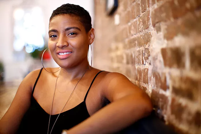 A smiling woman poses next to a brick wall