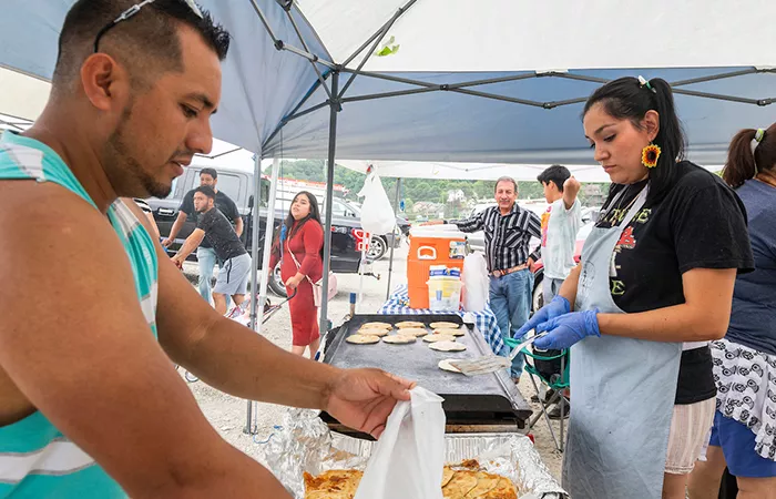 A man packs up pupusas while a woman grills them outside.