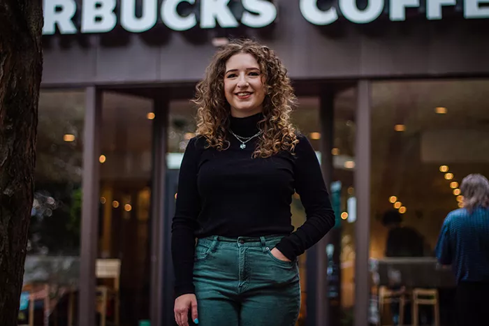 A woman smiling in front of a store with a "Starbucks Coffee" sign above the door