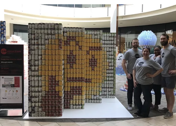 Several people stand next to a sculpture of Pac-Man made entirely from cans of food.
