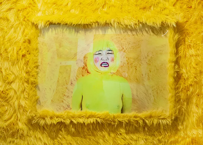 A woman in a yellow wig and body suit cries framed with yellow fur.