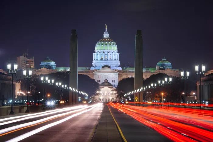 Harrisburg capitol building lit up at night, with a dark sky and bright white and red lights on the street