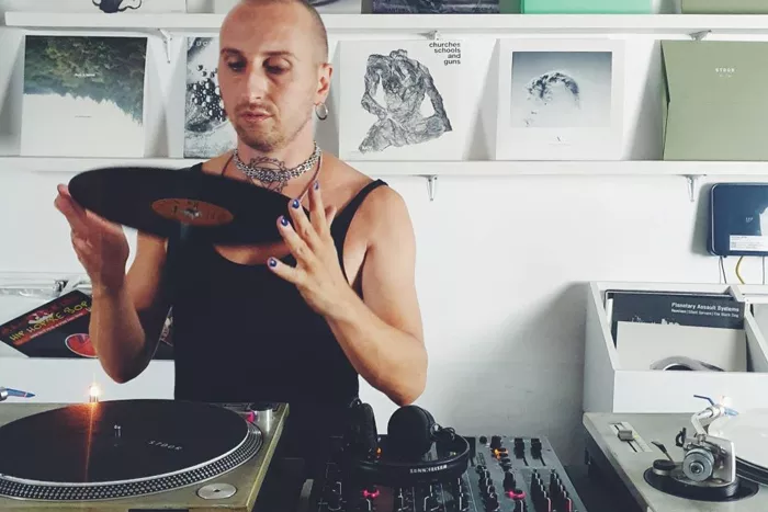 A DJ inspects a record as they stand by a turntable.