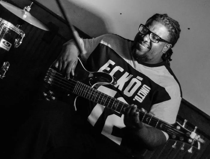 A black-and-white photo of a smiling Black man playing a guitar