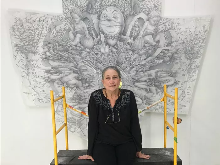 Woman in all black sits in front of an intricately drawn black-and-white illustration