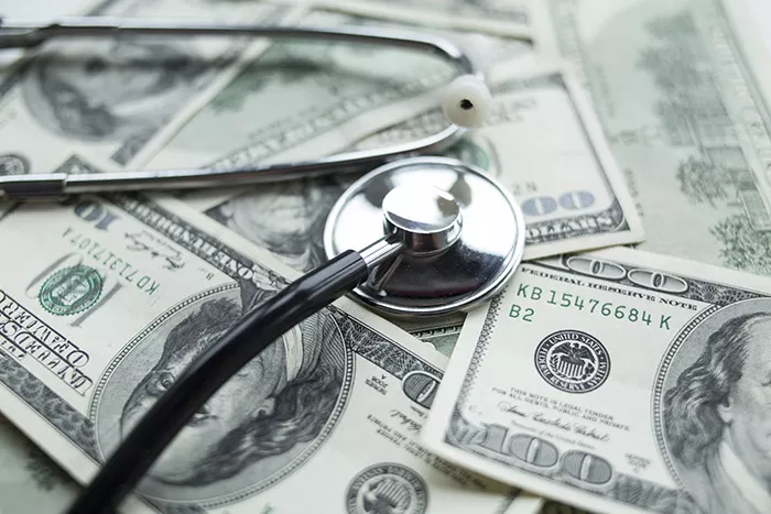 A stethoscope laying on top of a pile of $100 bills