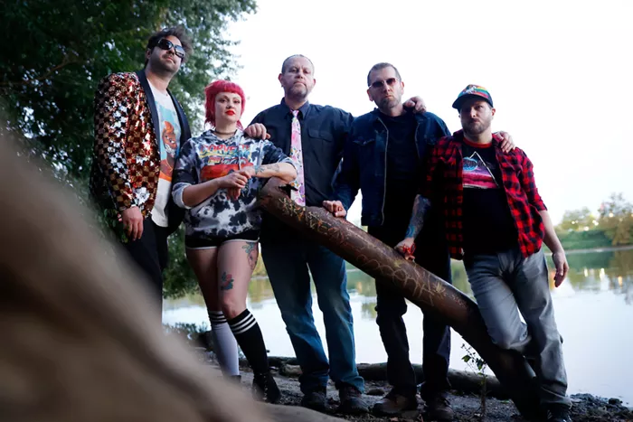 Five people stand together on the bank of a river