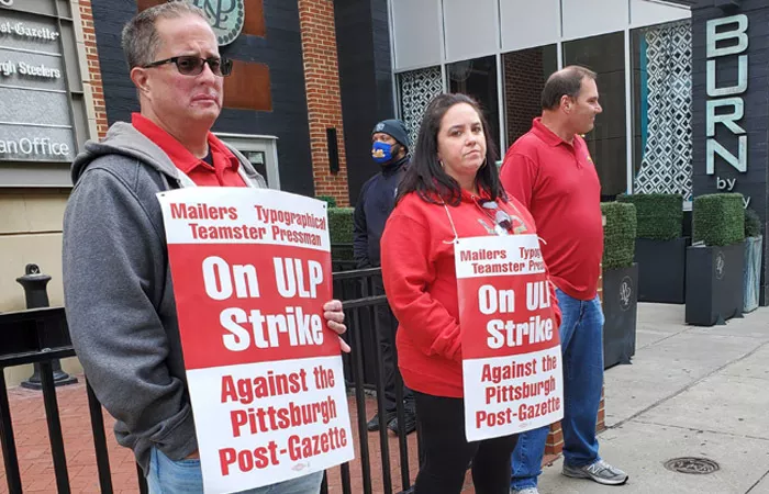 People stand outside the Pittsburgh Post-Gazette building holding up signs that say "On ULP Strike against the Pittsburgh Post-Gazette"