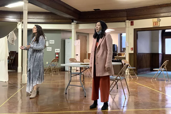 Two women stand in a room singing