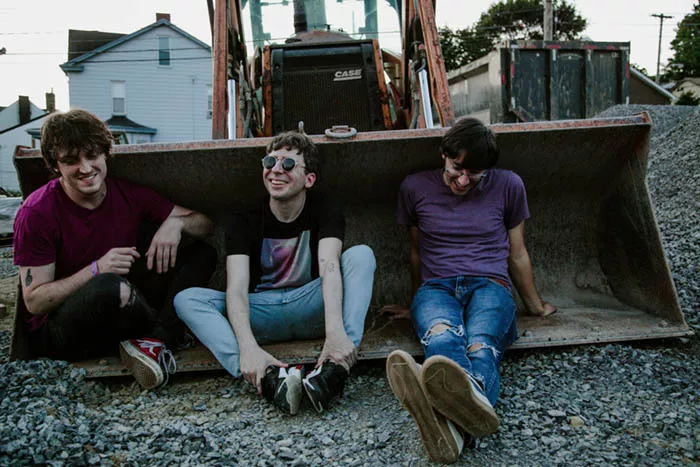 Three men sit in the bucket of a piece of construction equipment.