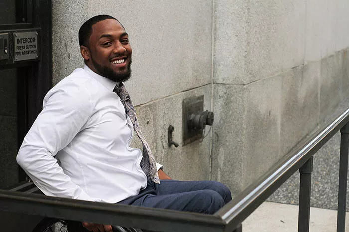 A young Black man in a wheelchair smiles at the camera.