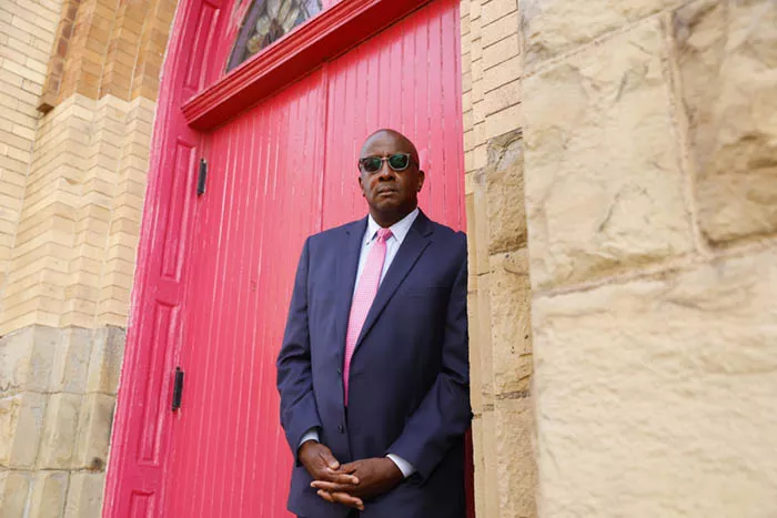 A man stands in front of red double doors