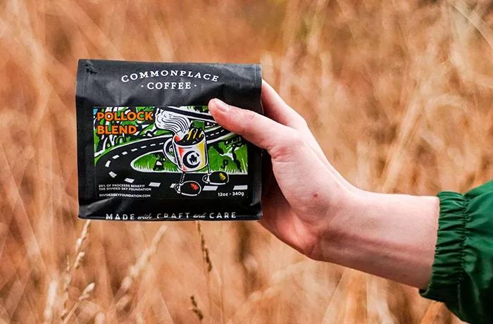 A hand holds a black bag of coffee featuring an artistic label.