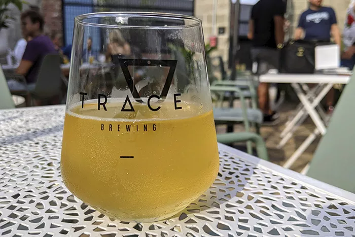 Close up of a half-empty glass of beer sits on a white metal table on the outdoor patio of Trace Brewing