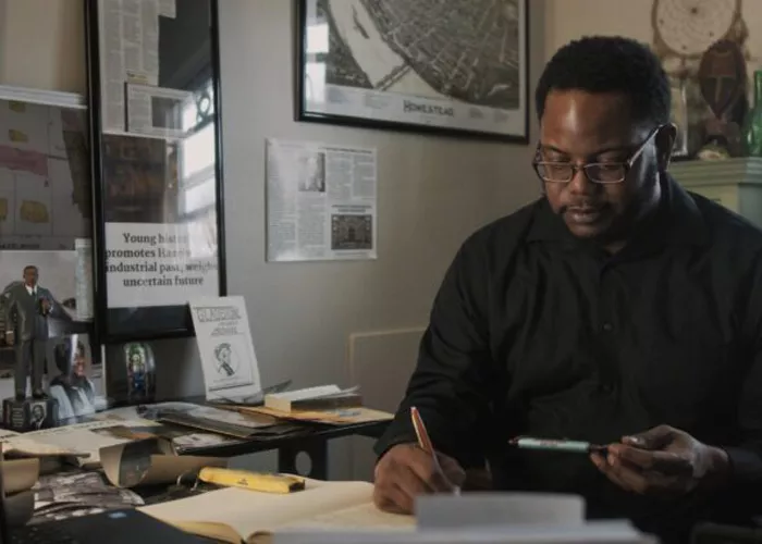 A Black man wearing glasses works at a desk.