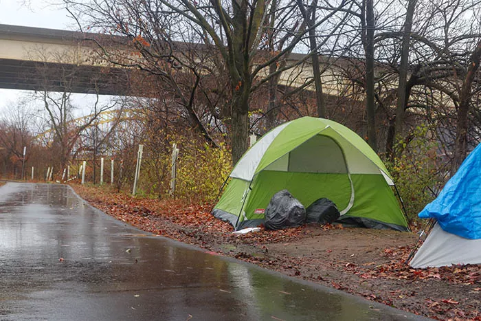A green tent set up in the woods near a path
