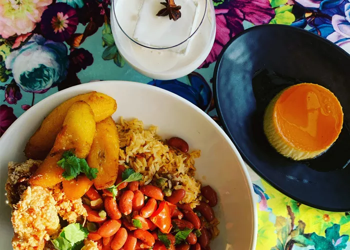 Close up of a Puerto Rican holiday dinner complete with beans and plantains, flan, and a milky white cocktail.