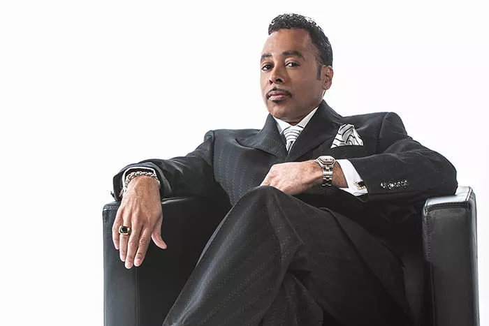 A distinguished Black gentleman looks at the camera as he sits in a chair.