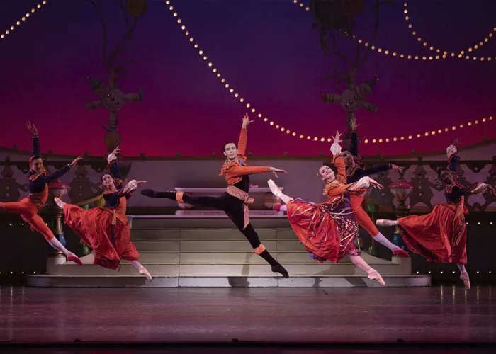 A group of ballet performers in vivid red costumes jump and spin on stage.
