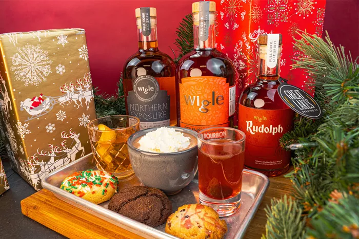 A colorful display of cocktails, cookies, and whiskey bottles surrounded by festive holiday decor.