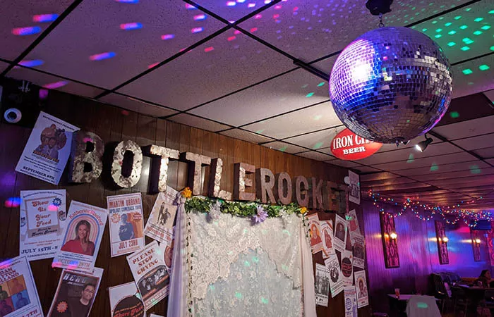 A disco ball casts multicolored spots of lights on the walls of a dive bar.