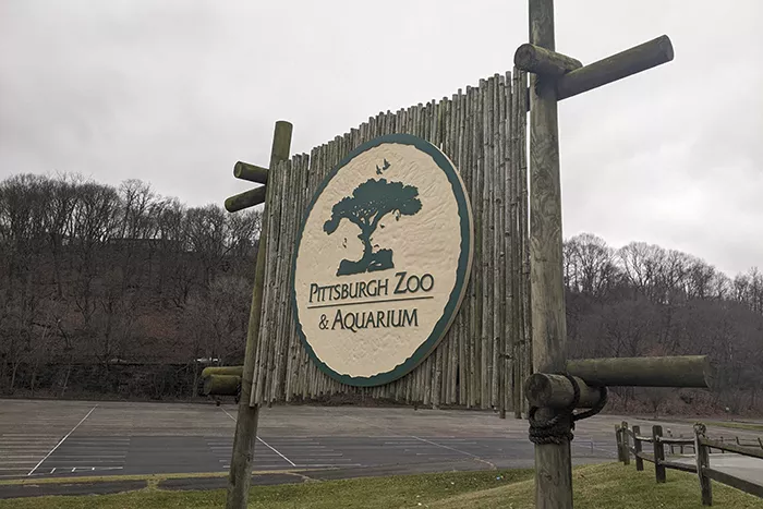 A sign reading "Pittsburgh Zoo and Aquarium" sits at the end of a vast parking lot on an overcast day.