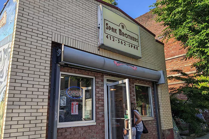 Two people enter the storefront of Spak Brothers pizza shop on a clear, sunny day.