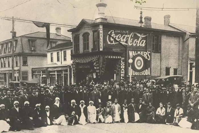 A black and white archival photo shows a large group of Black men and women dressed in suits and medical gear.