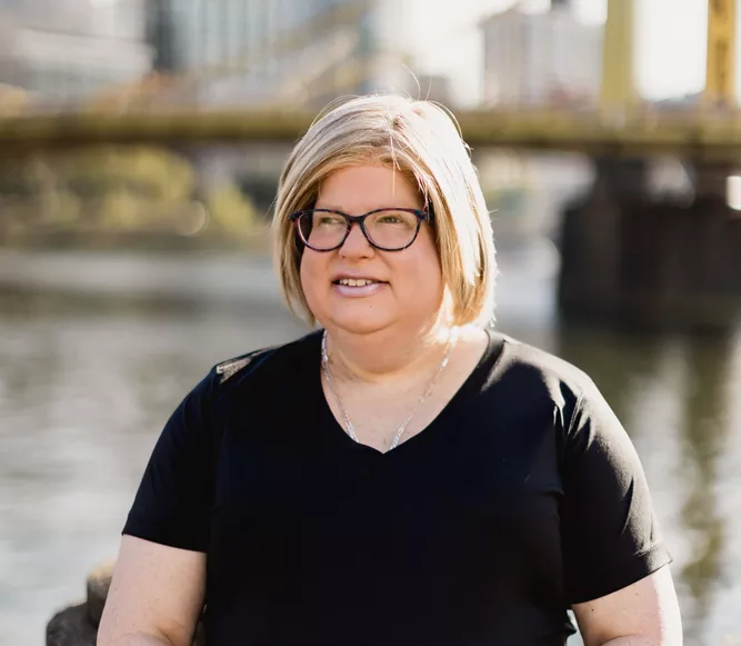 Brett Wilson has shoulder-length blond hair and glasses and stands by the Three Sisters bridges in casual black clothing.