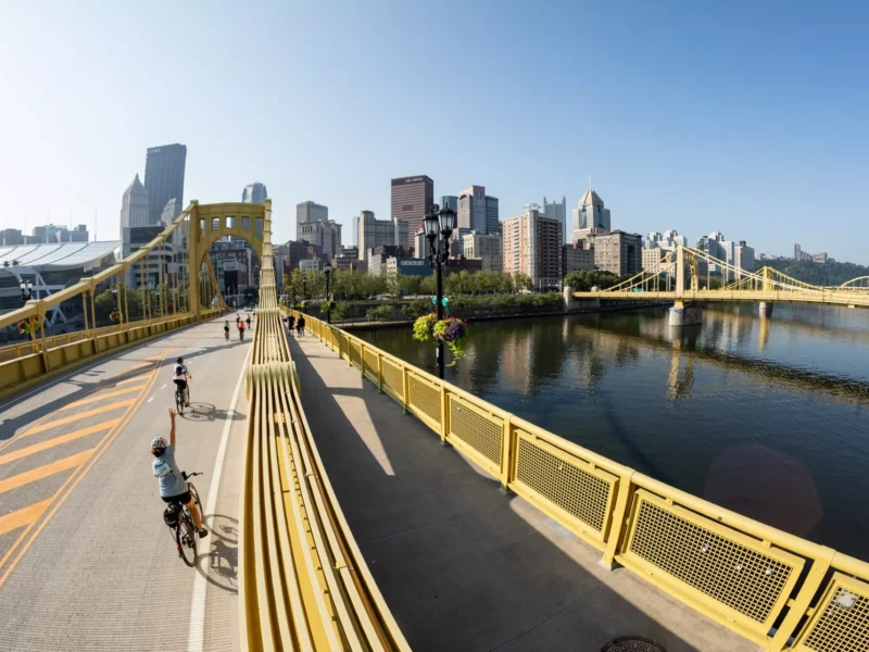 Cyclists ride across a car-free Roberto Clemente Bridge with the Pittsburgh skyline in background