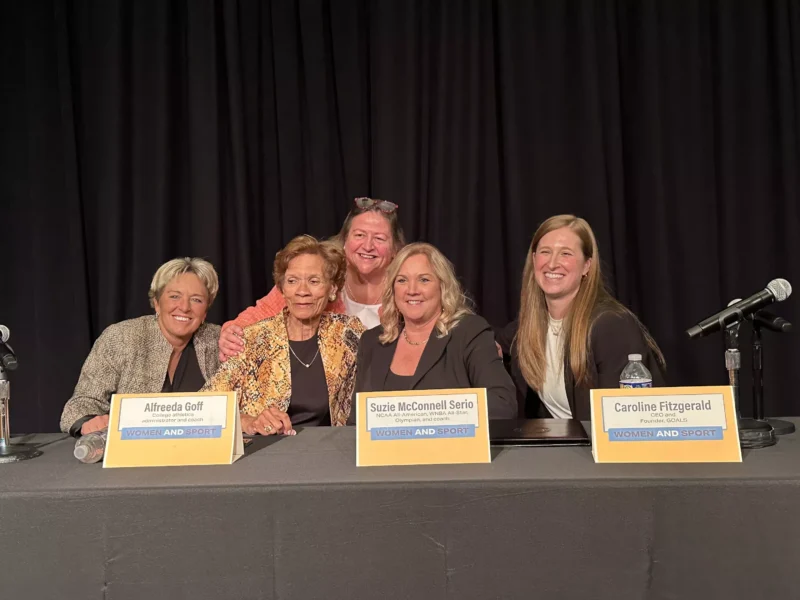 Four women sit smiling behind nametags at a table on a stage