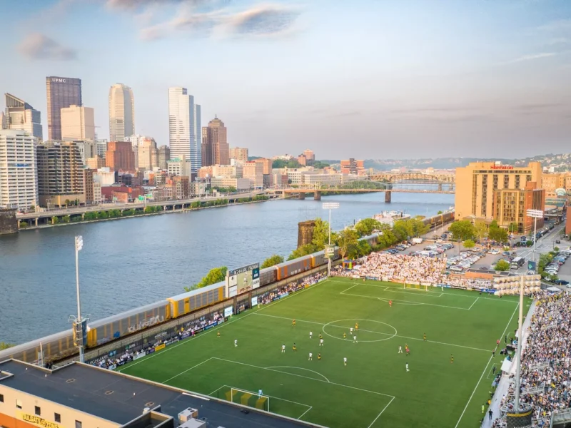 A small soccer stadium sits across a wide river from Pittsburgh's skyline