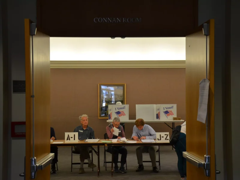 Three poll workers discuss ballots in a small room