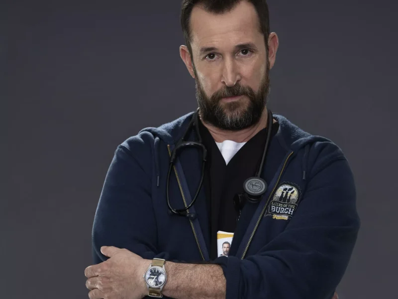 Noah Wyle in scrubs wearing a stethoscope and Beers of the Burgh hoodie