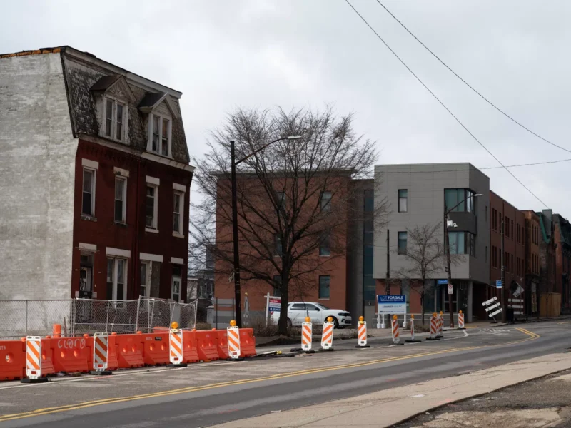 Three-story gabled brick houses sit behind chain-link fencing near an aluminum-paneled midrise building