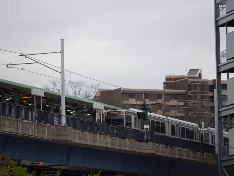 A T streetcar on a concrete overpass with electric wires over head and the Modernist buildings of CCAC behind