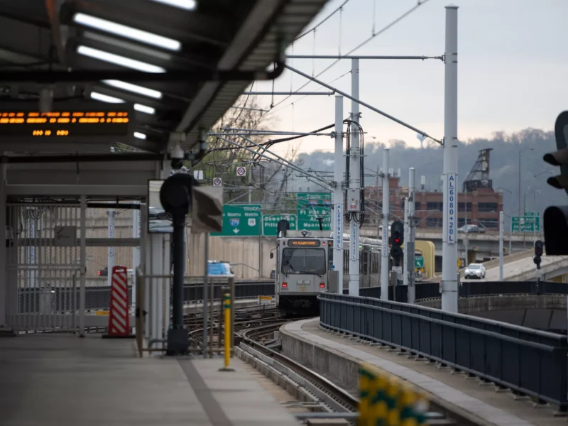 A streetcar departs an elevated concrete station with LED signs indicating the next departure time