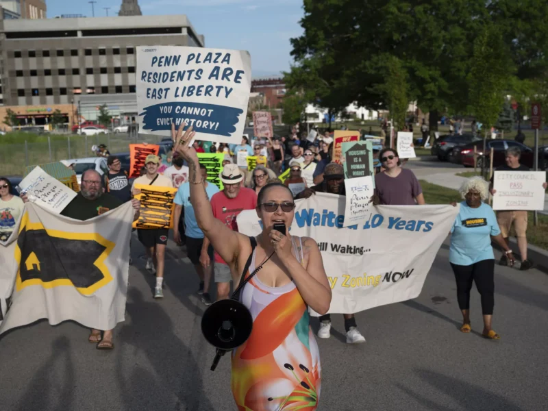 A crowd of people holding handmade and printed placards marches down one side of a four-lane street