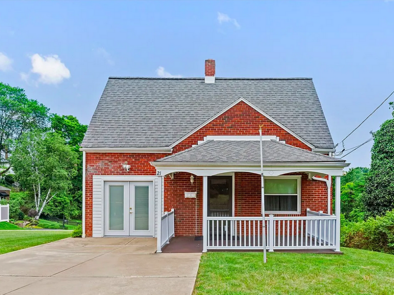 A small red brick cottage-style house with white trim and a small centered chimney