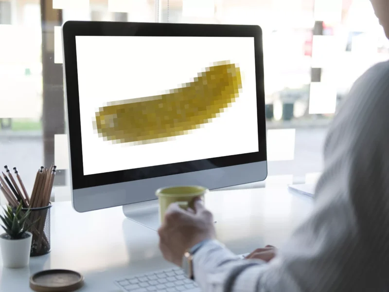 A man sits at an office computer displaying a pixelated pickle.