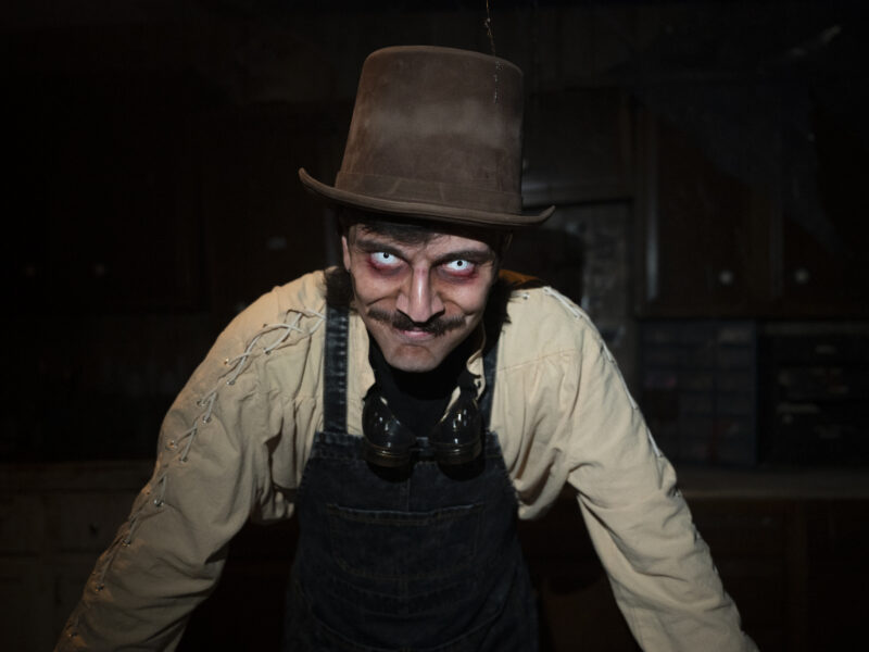A man with creepy colored contacts in a dirty top hat leers at the camera