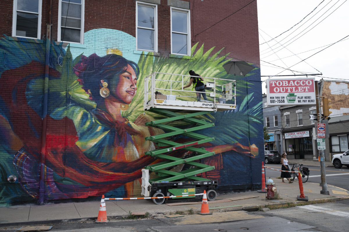 An artist works on a story-high mural of a woman dancing with lit candles