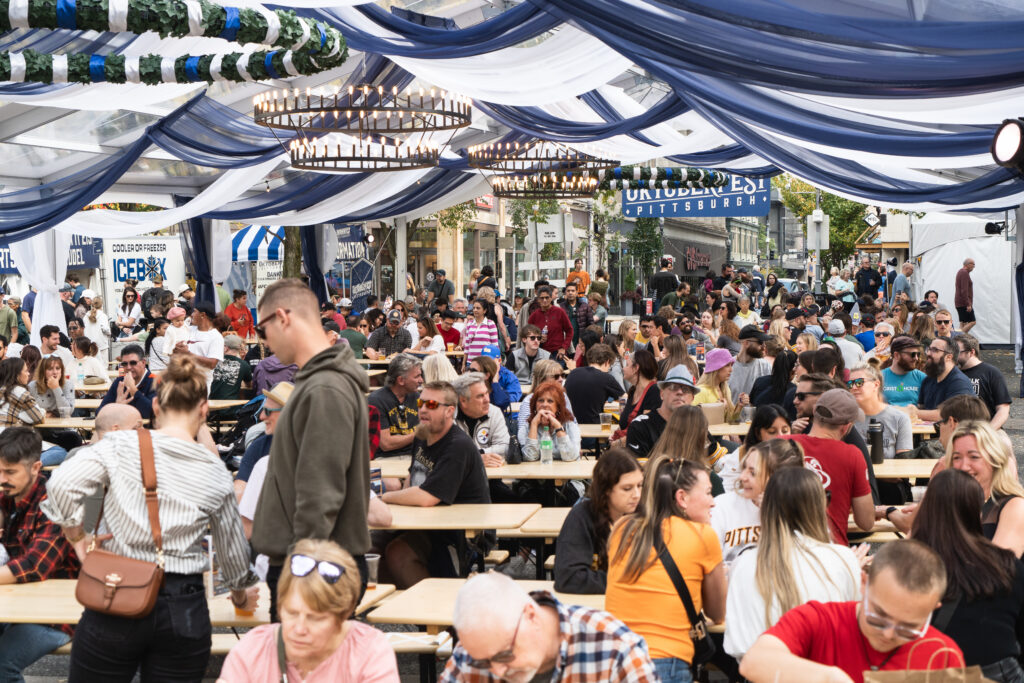 A large crowded tent with traditional wreaths hangs over a downtown street