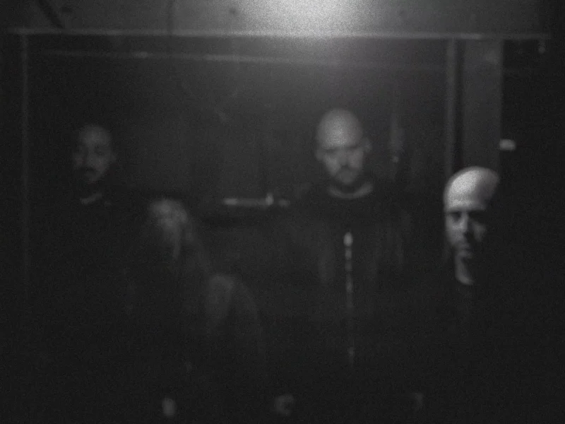 A band of four in dark clothing in a dimly lit room