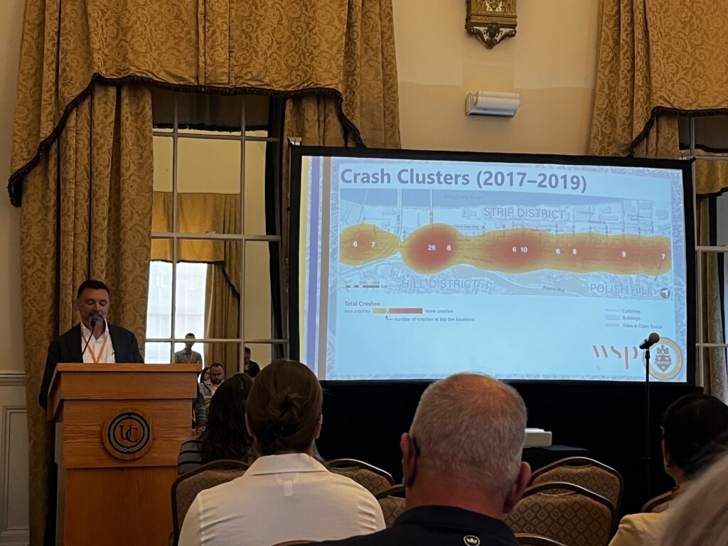 A man in a suit without a tie gives a presentation before ornate gold curtains