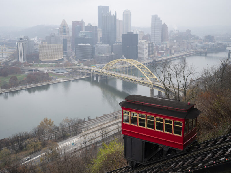 A trolley-like funicular descends against a backdrop of the Pittsburgh skyline
